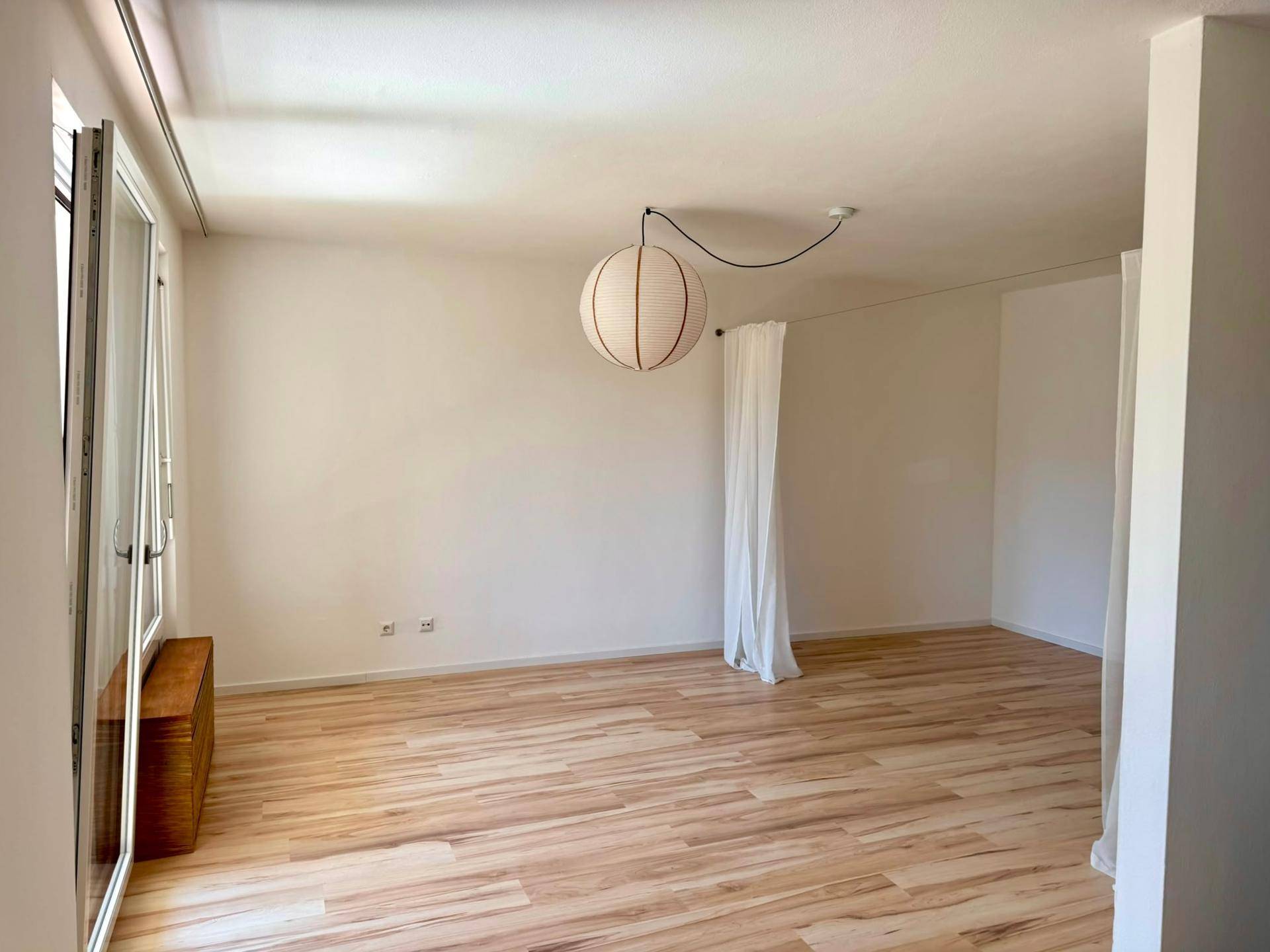 Heller Wohnbereich mit Laminatboden und einem Fenster, das viel Tageslicht hereinlässt.