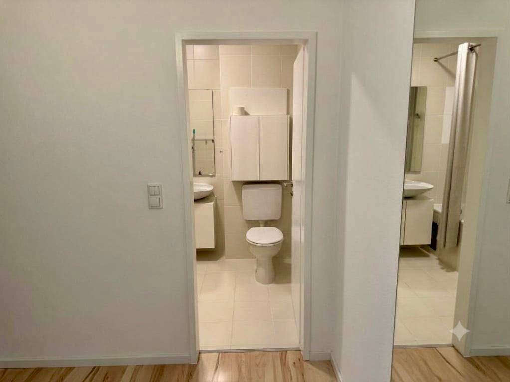 Zwei Badezimmerbereiche mit hellen Fliesen, Waschbecken und Toilette.