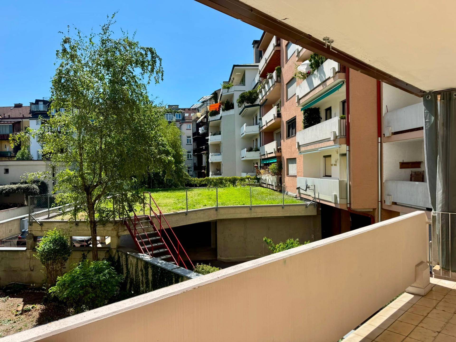 Balkon mit Blick auf die umliegenden Gebäude und eine begrünte Gemeinschaftsfläche.