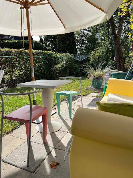 Sonniger Terrassenbereich mit Gartenmöbeln, großem Sonnenschirm und Blick ins Grüne.