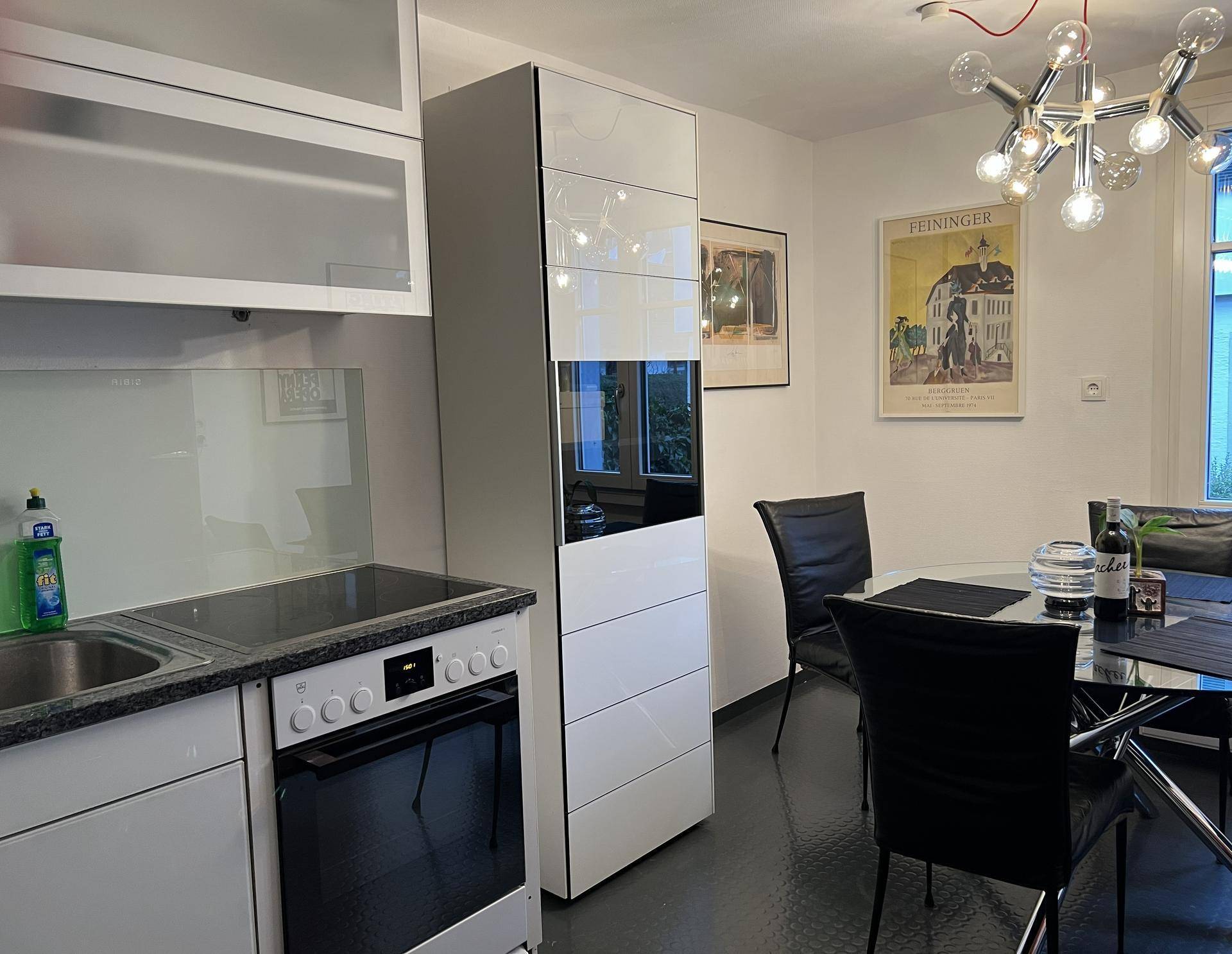 Moderne Küche mit weißen Hochglanzschränken, integriertem Backofen und Essbereich.