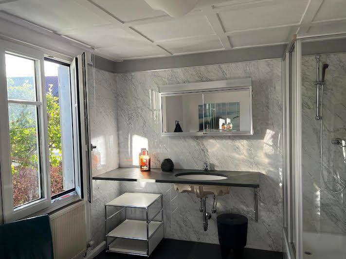 Modernes Badezimmer mit Dusche, Einzelwaschbecken, Spiegelschrank und Fenster für Tageslicht.