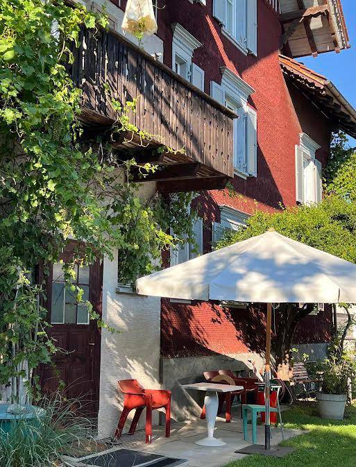 Gemütliche Terrasse vor dem roten Haus mit Gartenmöbeln und üppiger Bepflanzung.