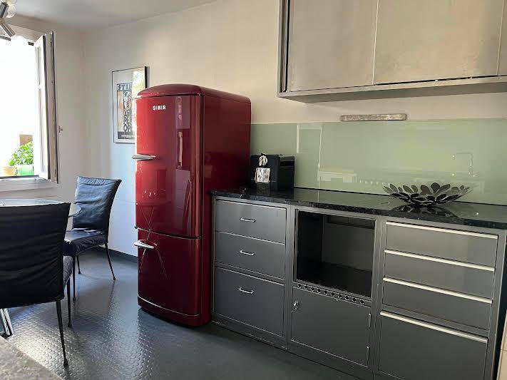 Küche mit rotem Retro-Kühlschrank, grauen Unterschränken und einem Essbereich am Fenster.