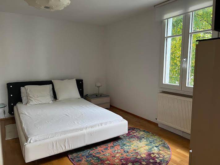 Helles Schlafzimmer mit Holzboden, weißem Bett, farbigem Teppich und großem Fenster.