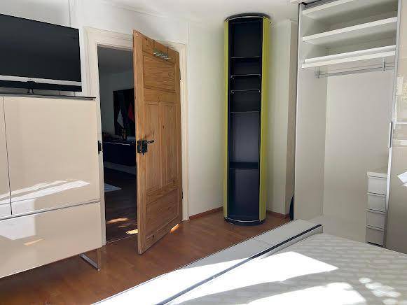 Schlafzimmer mit Holzboden, offenem Kleiderschrank und einer Holztür, die in einen anderen Raum führt.