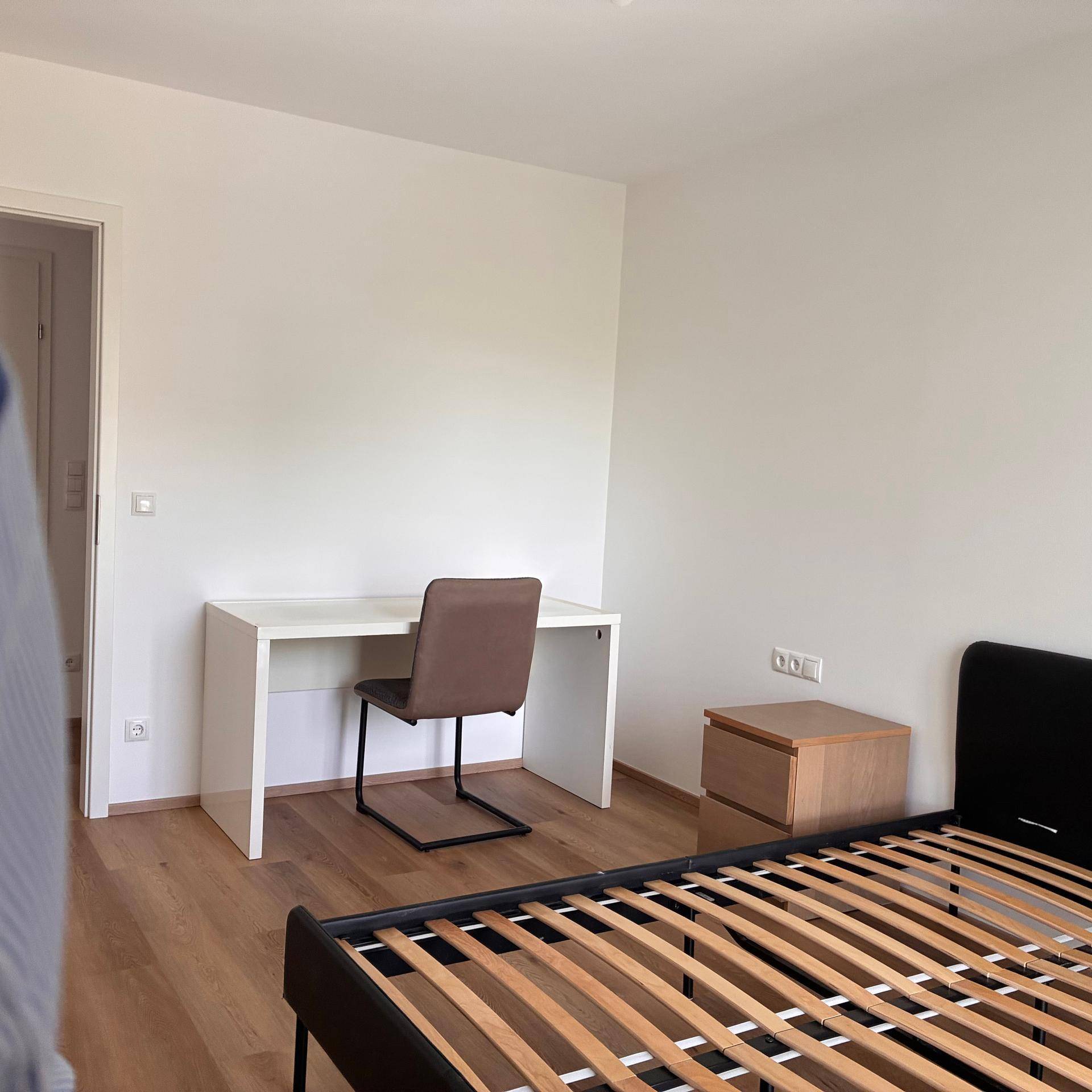 Schlafzimmer mit Parkettboden, Bettgestell und einem Arbeitsbereich mit Schreibtisch.