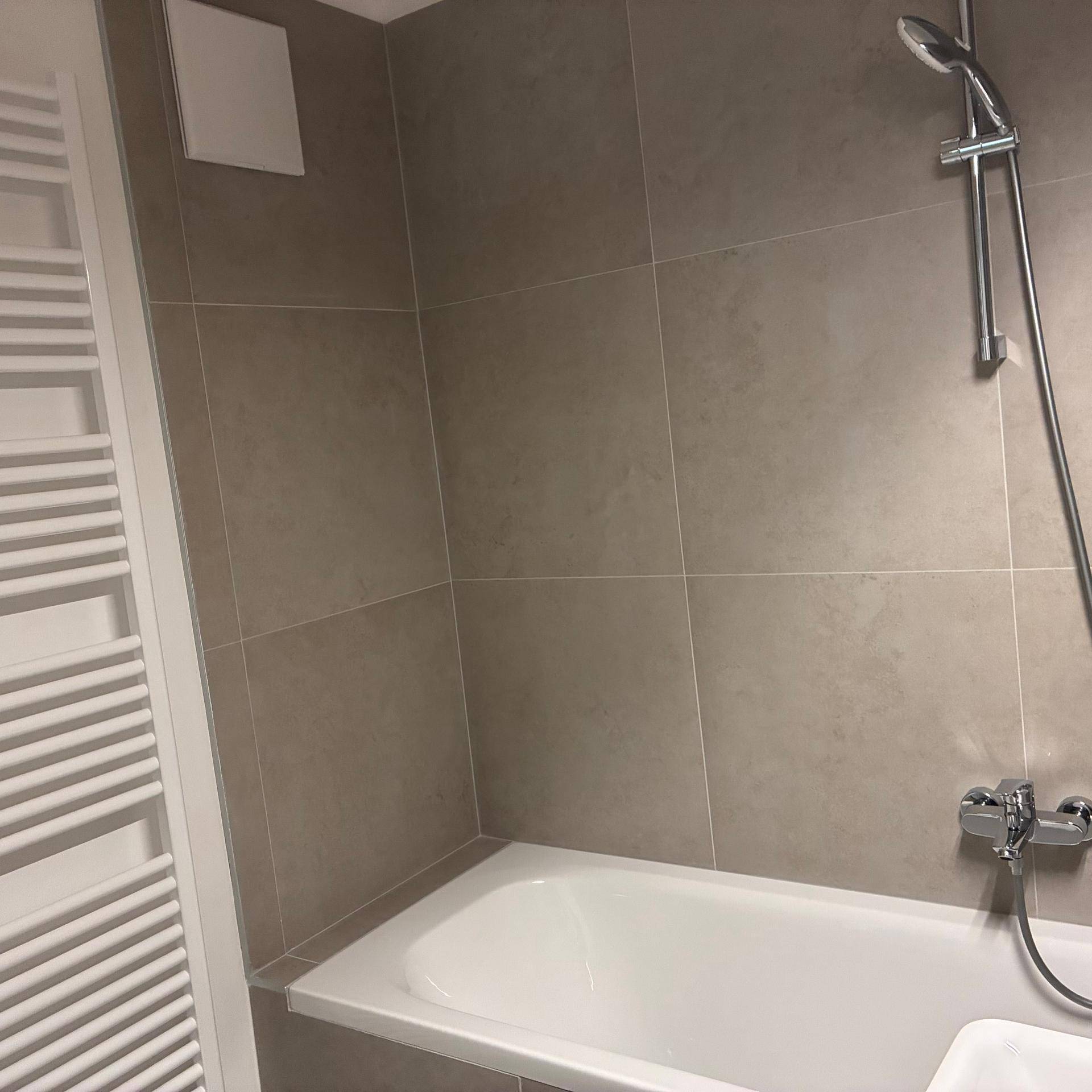 Badewanne mit Duscharmatur und beheiztem Handtuchhalter in modern gefliestem Badezimmer.