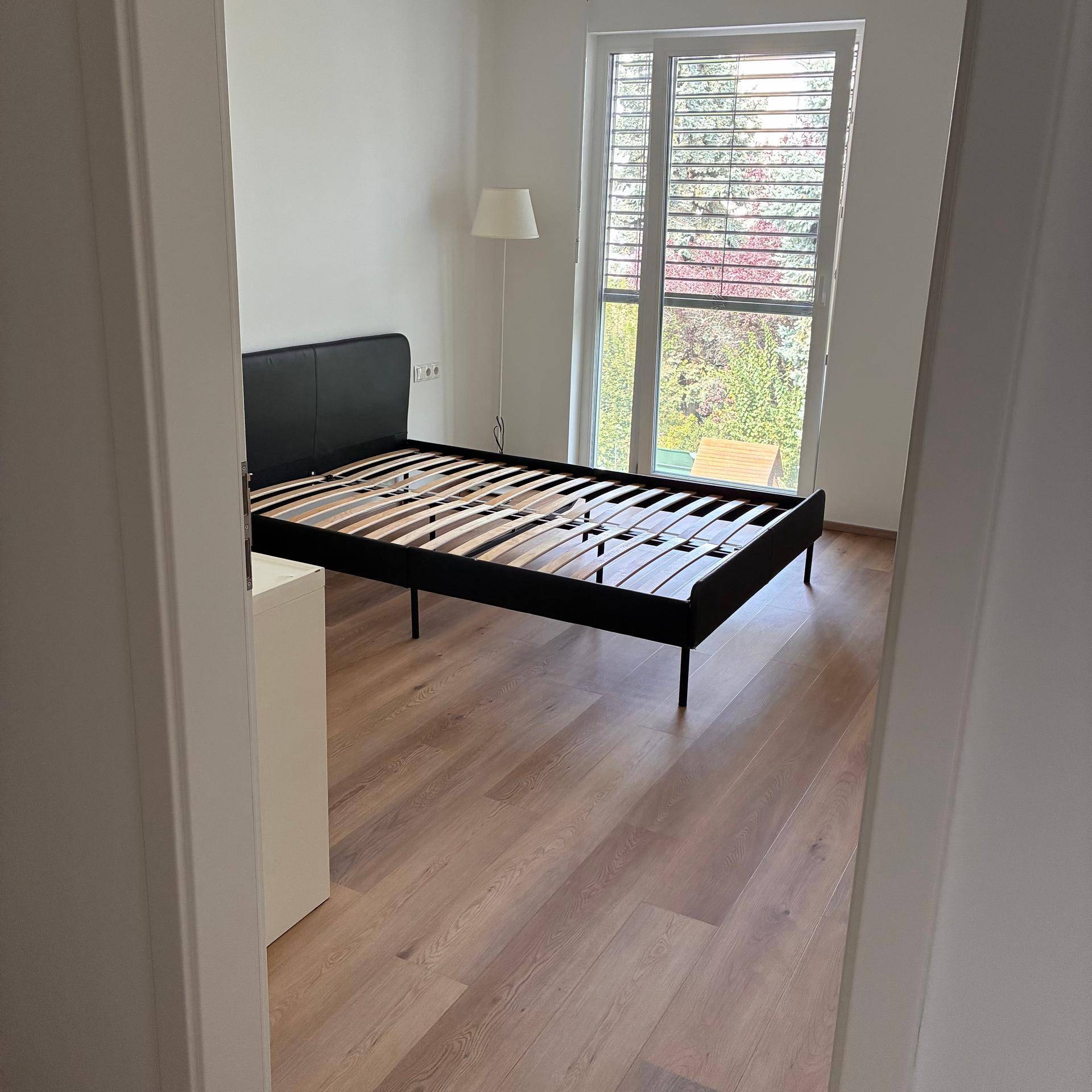 Schlafzimmer mit großem Fenster, das viel Tageslicht und einen Blick ins Grüne bietet.