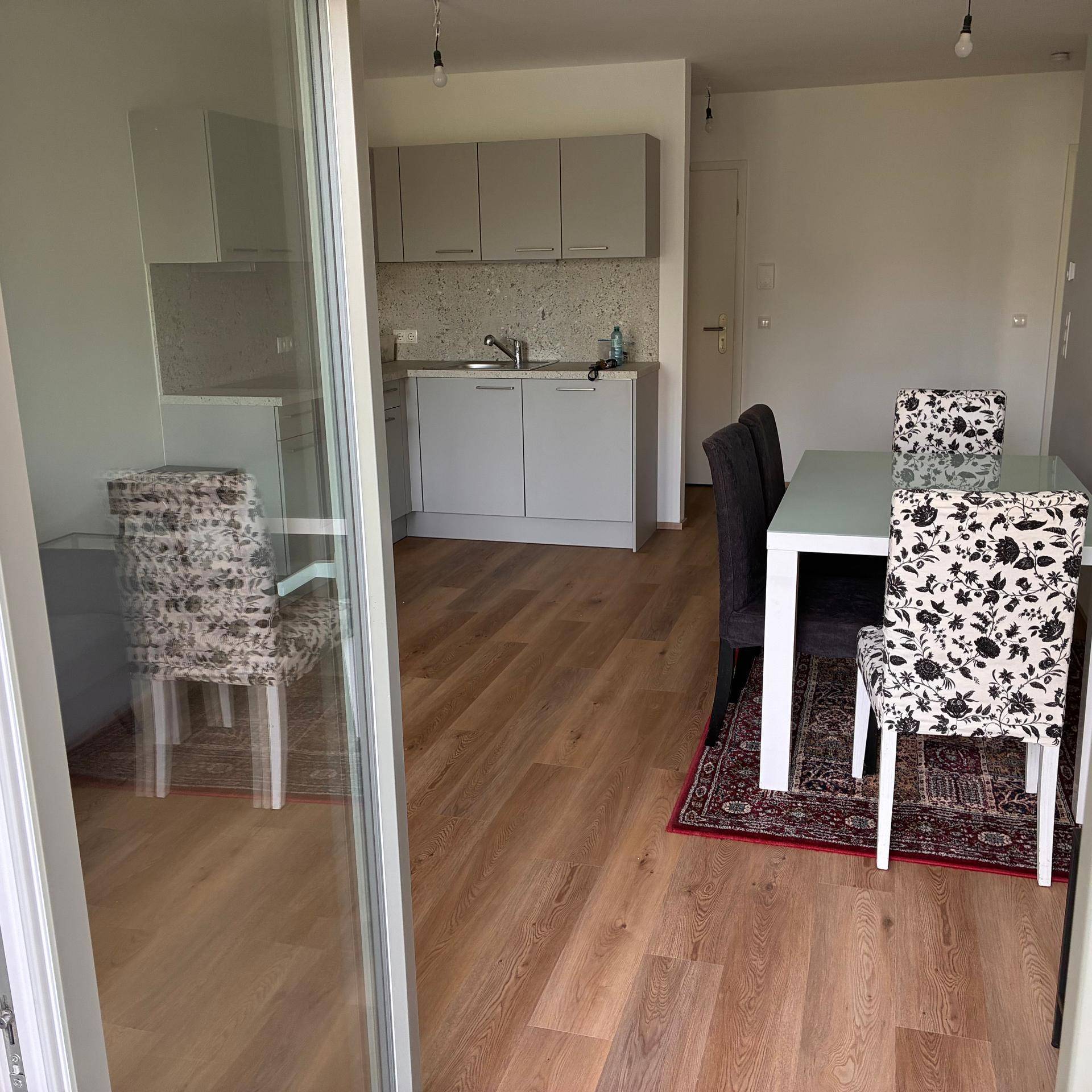 Heller Wohn- und Essbereich mit Parkettboden und moderner Küchenzeile, vom Balkon aus gesehen.
