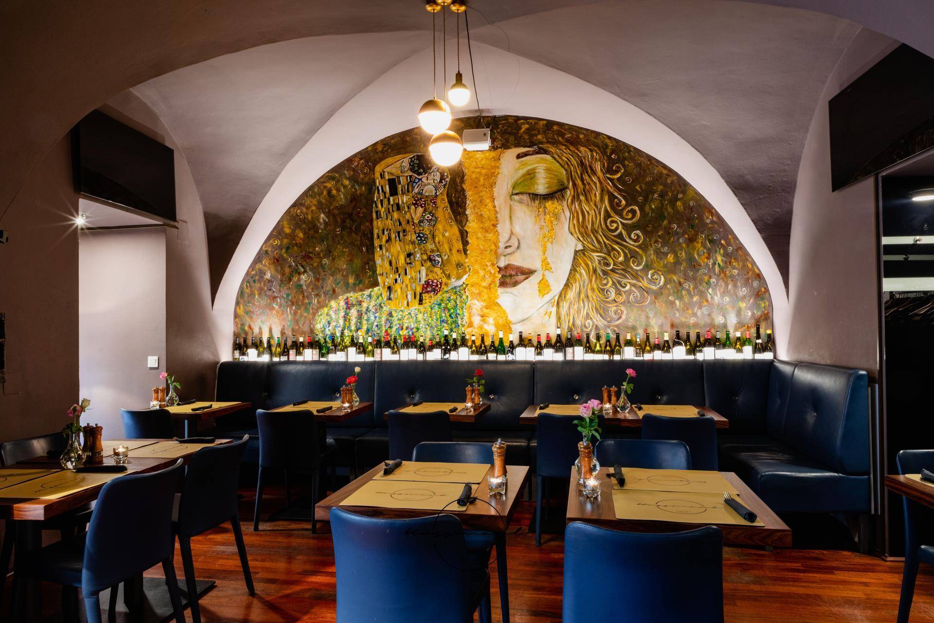 Gemütlicher Restaurantbereich mit gewölbter Decke, großem Wandgemälde und Sitzbänken entlang der Wand.
