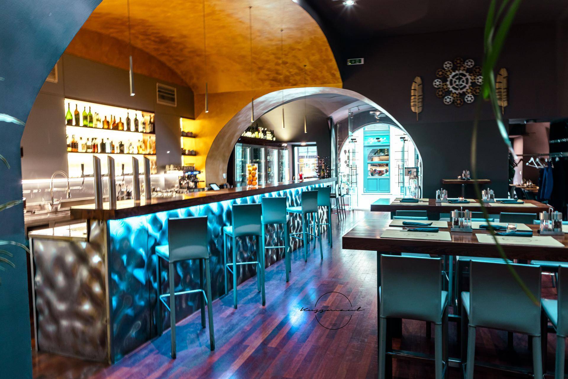 Moderne Bar mit beleuchteter Theke, Barhockern und Holzboden in einem stilvollen Ambiente mit historischen Bögen.