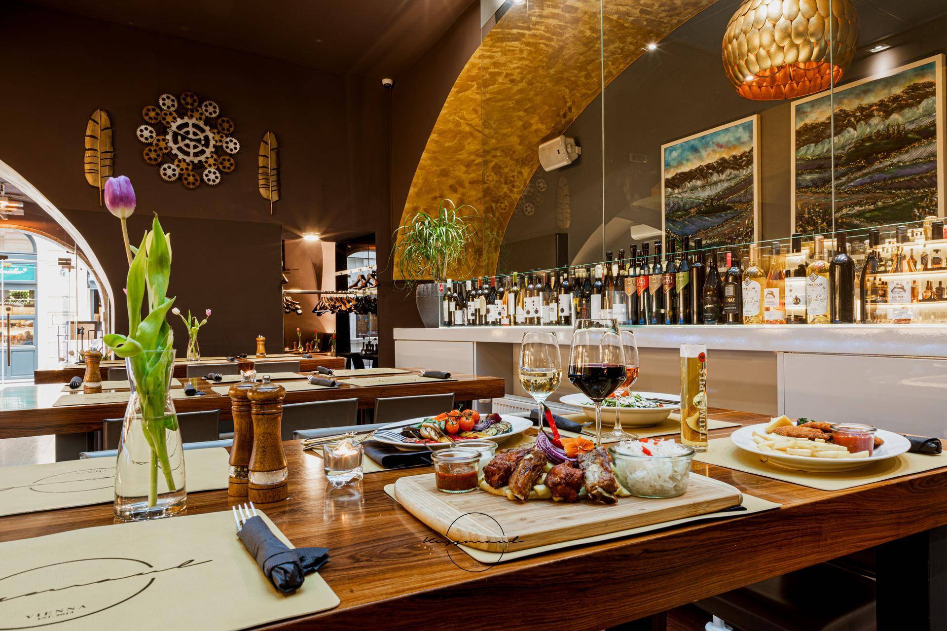 Gedeckter Tisch mit Speisen und Getränken in einem eleganten Restaurant mit Holzboden und stilvoller Dekoration.