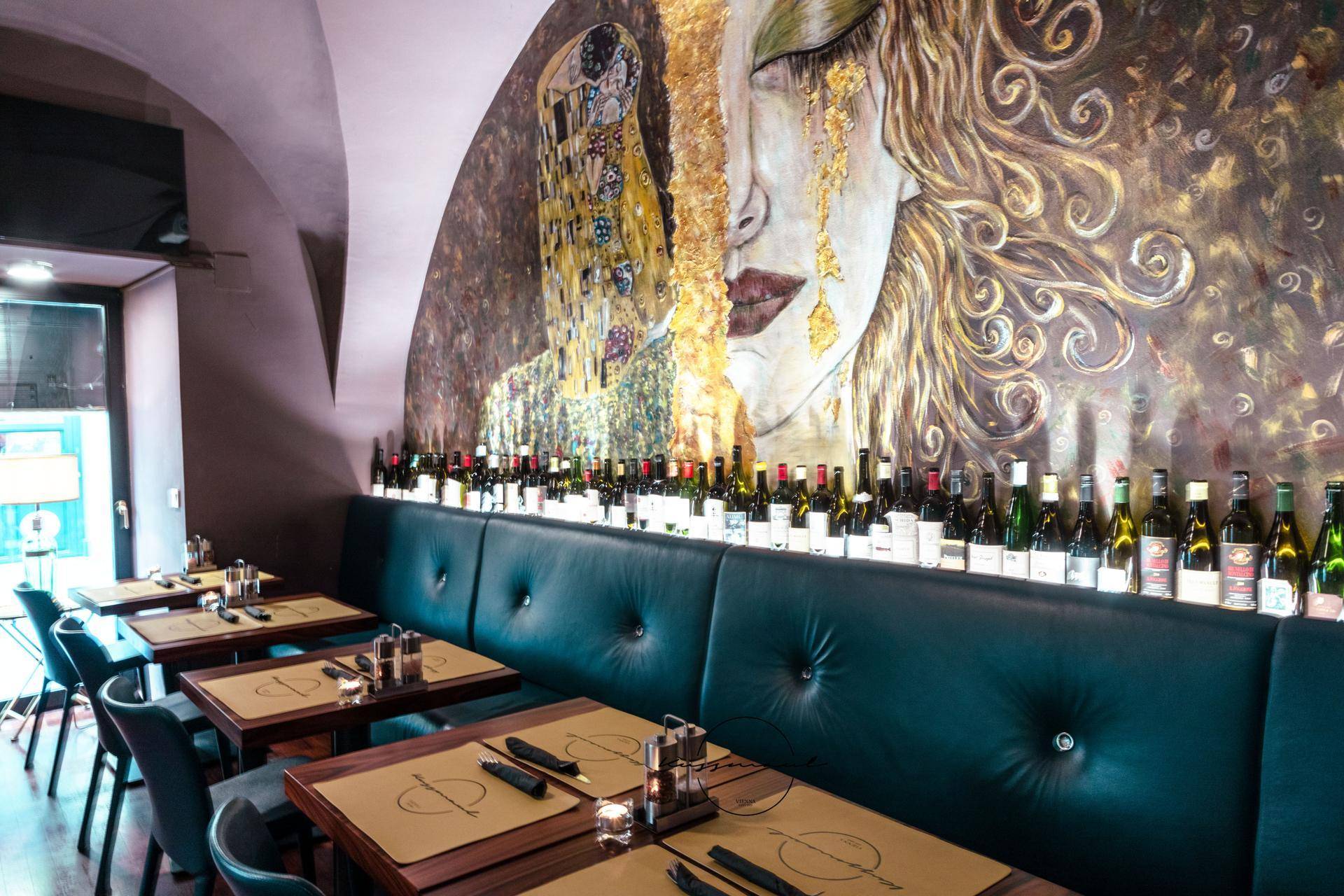 Nahaufnahme des kunstvollen Wandgemäldes und der bequemen Sitzbänke in einem eleganten Restaurant mit vielen Weinflaschen.