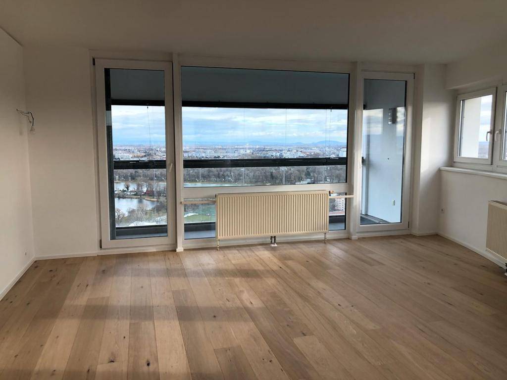 Geräumiges Wohnzimmer mit Holzboden und raumhohen Fenstern, die einen Panoramablick bieten.