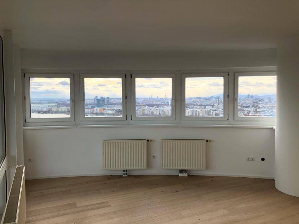 Heller Wohnbereich mit gebogener Fensterfront, Holzboden und weitem Blick über die Stadt.