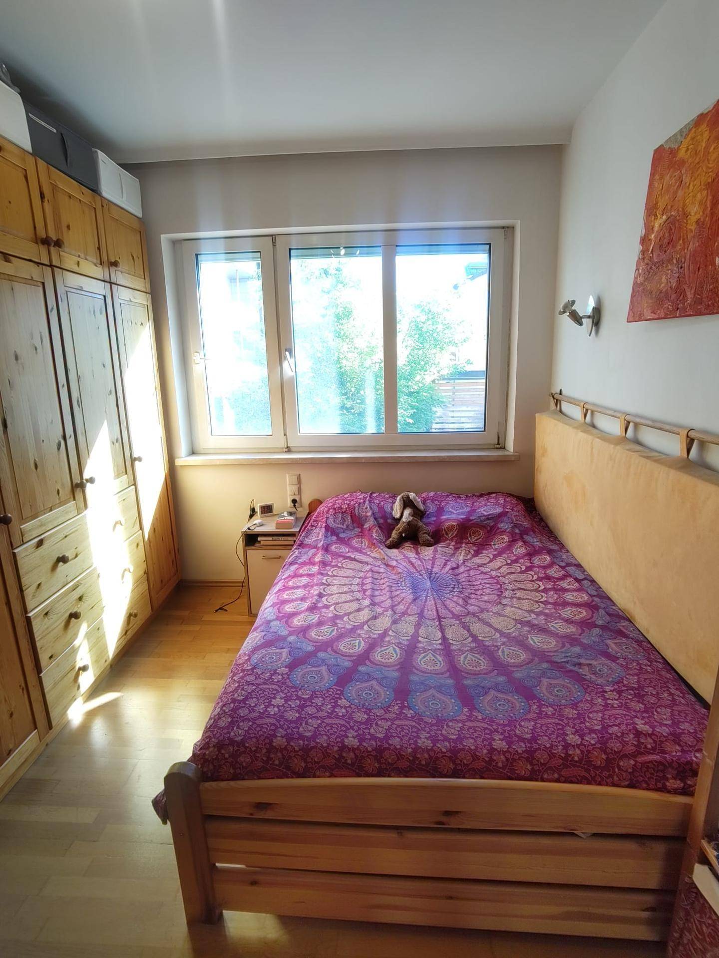 Helles Schlafzimmer mit Einzelbett, Holzschrank und viel natürlichem Licht durch das Fenster.