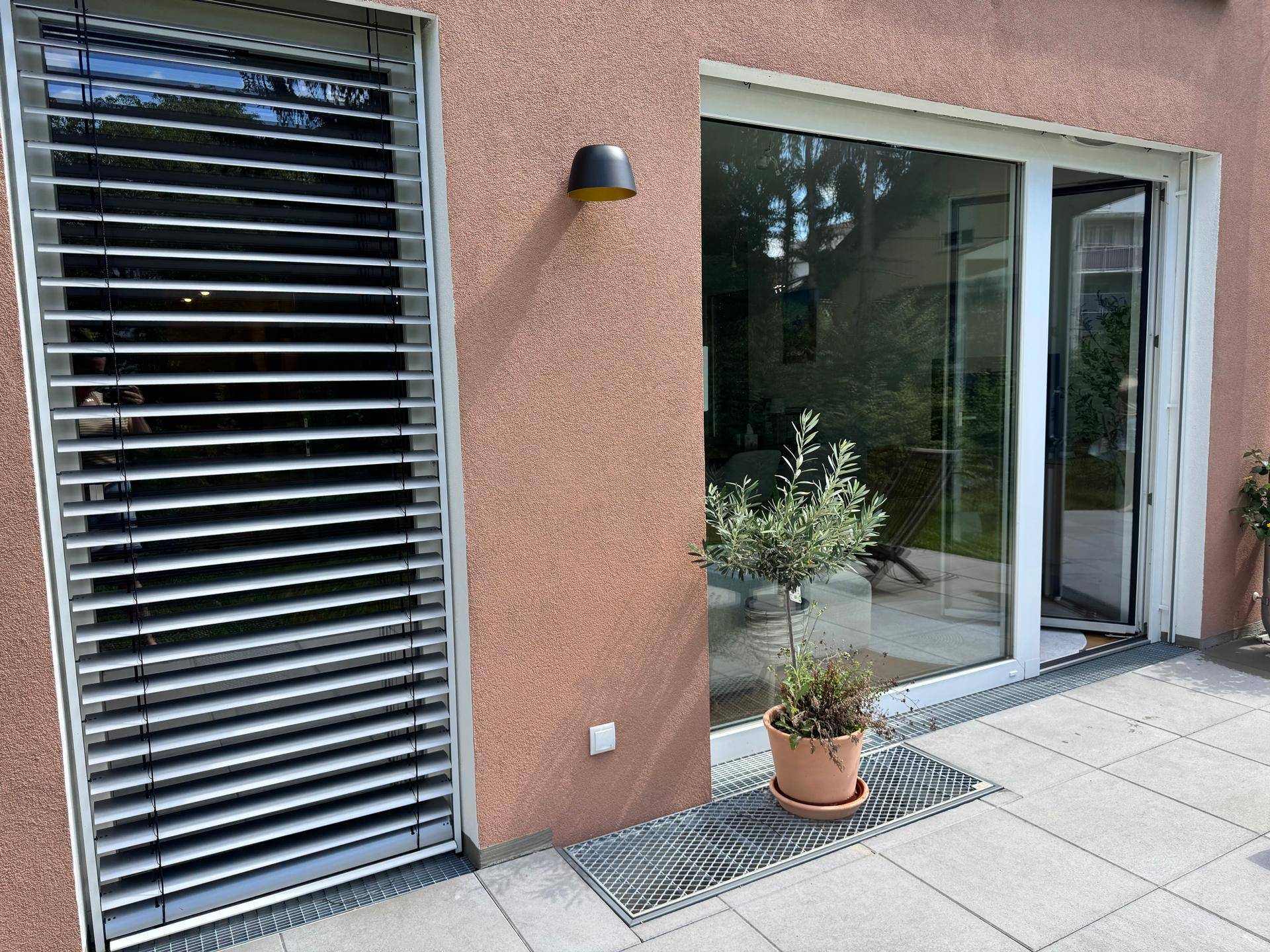 Detailansicht der Terrasse mit Topfpflanze und modernen Außenjalousien am Fenster.