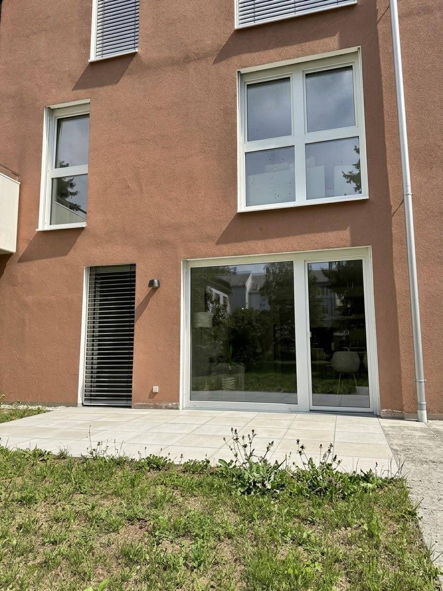 Außenansicht der Gebäudefassade mit einer gepflasterten Terrasse und Grünfläche.