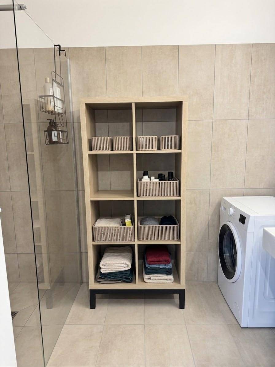 Badezimmer mit praktischem Regal, Waschmaschine und modernen Wandfliesen.