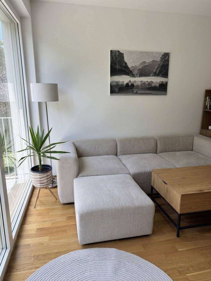 Gemütliches Wohnzimmer mit hellem Sofa, Holztisch und großen Fenstern für viel Licht.