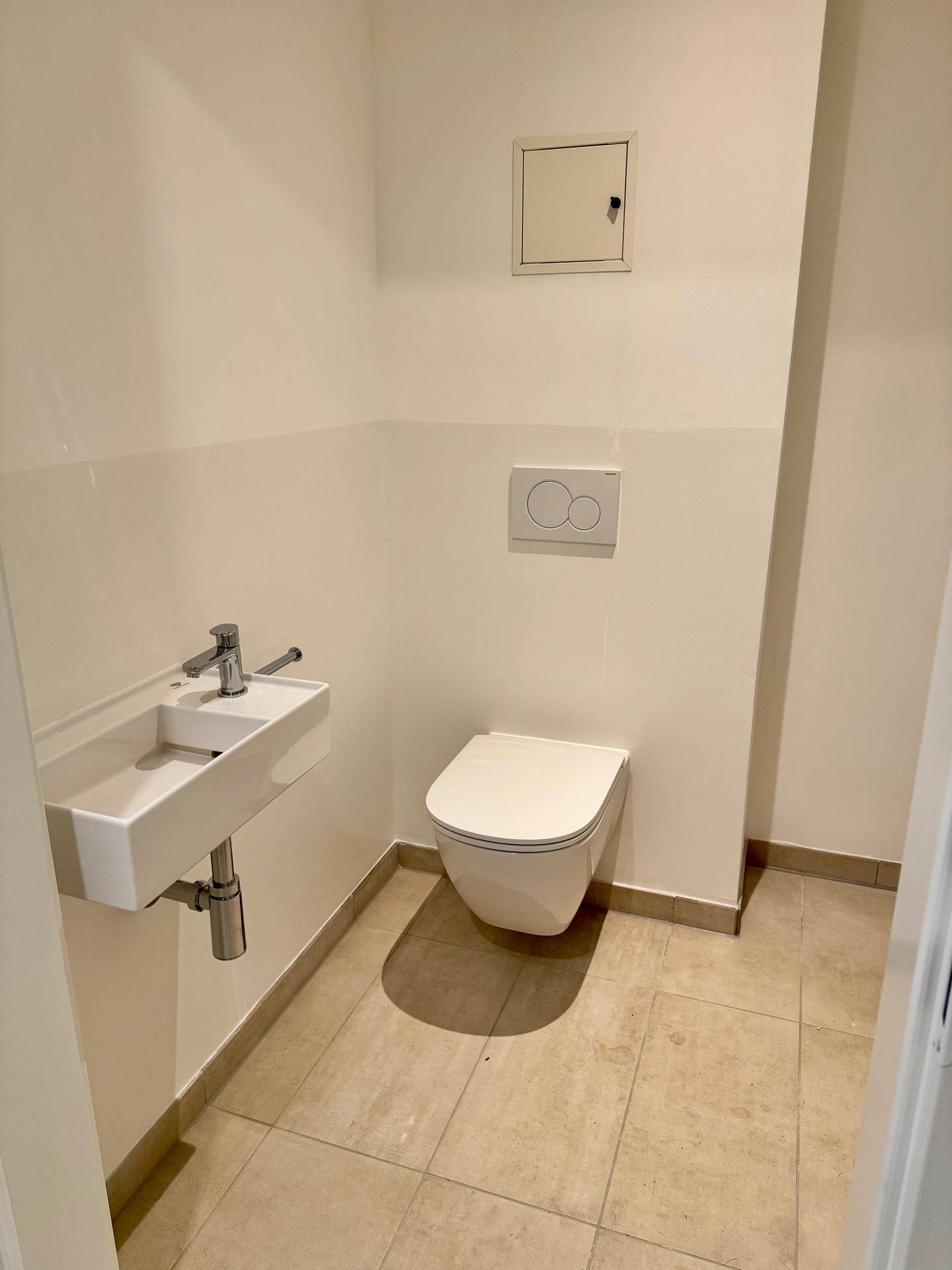 Modernes Gäste-WC mit wandhängender Toilette und kleinem Waschbecken in neutralen Farben.