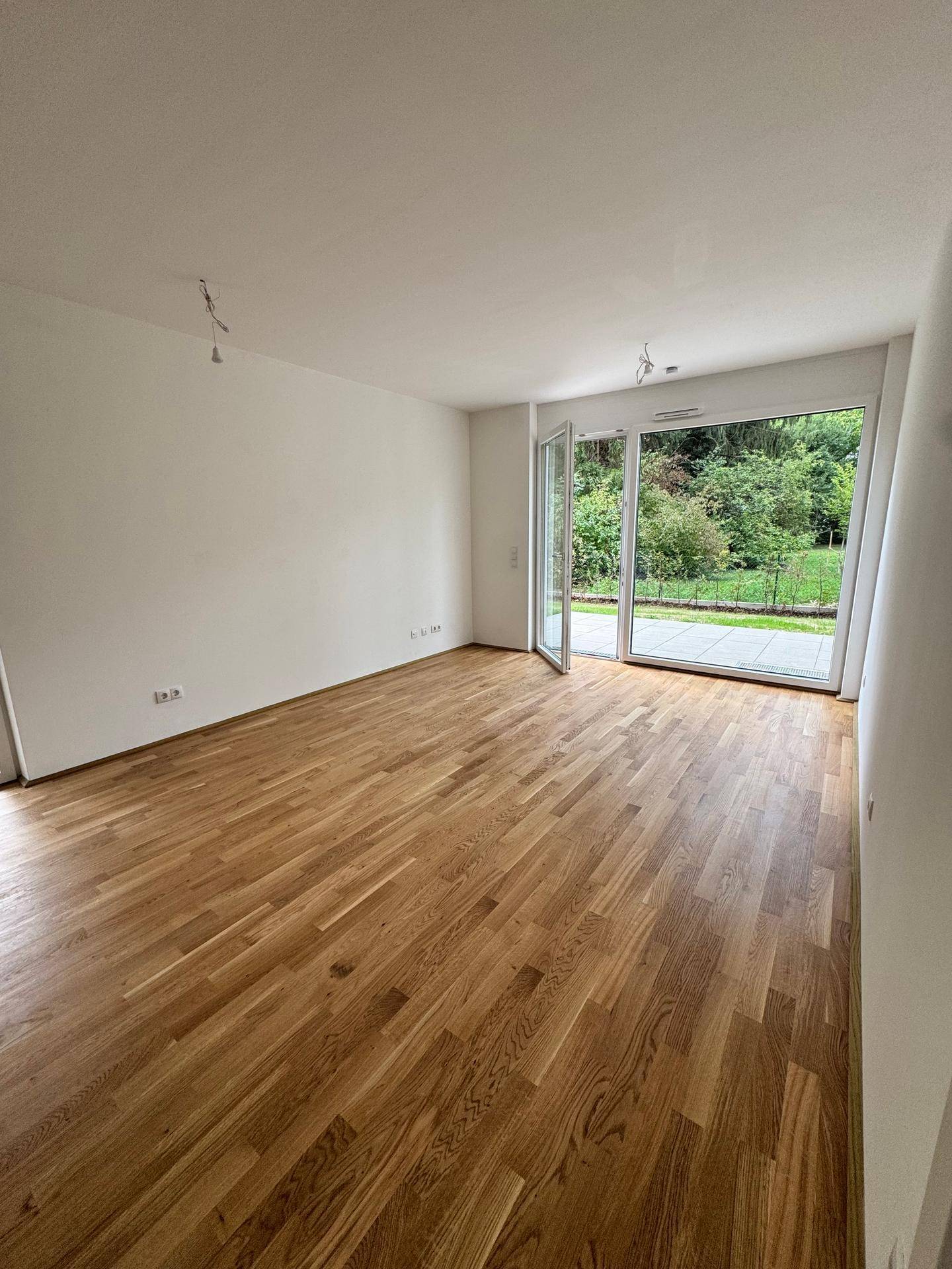 Geräumiges Zimmer mit Holzboden und großen Glastüren zum Außenbereich.