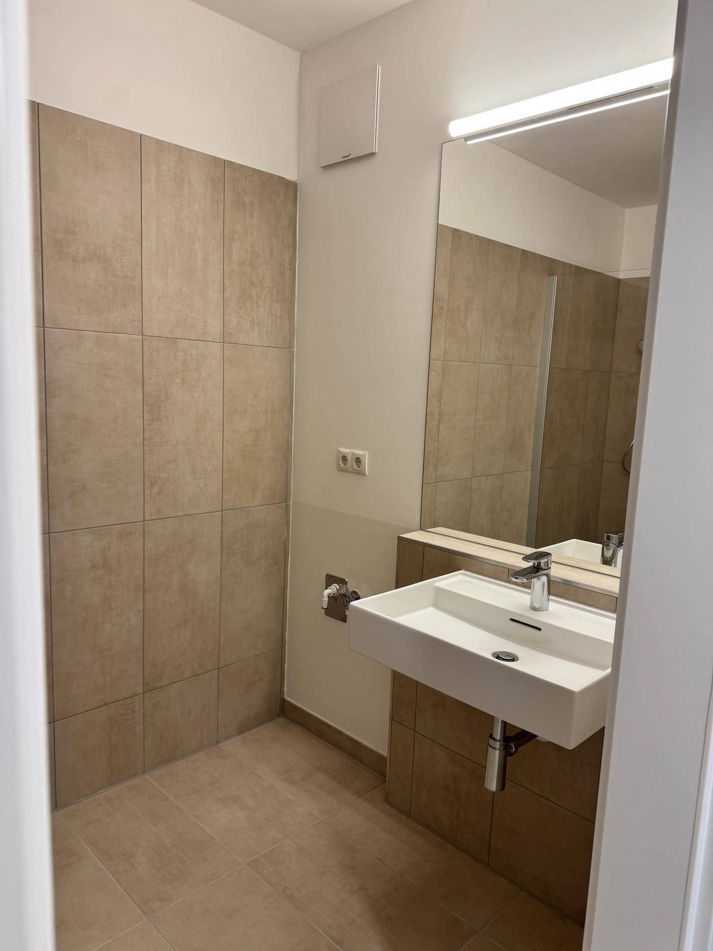 Modernes Badezimmer mit Waschbecken, großem Spiegel und hellen Fliesen.