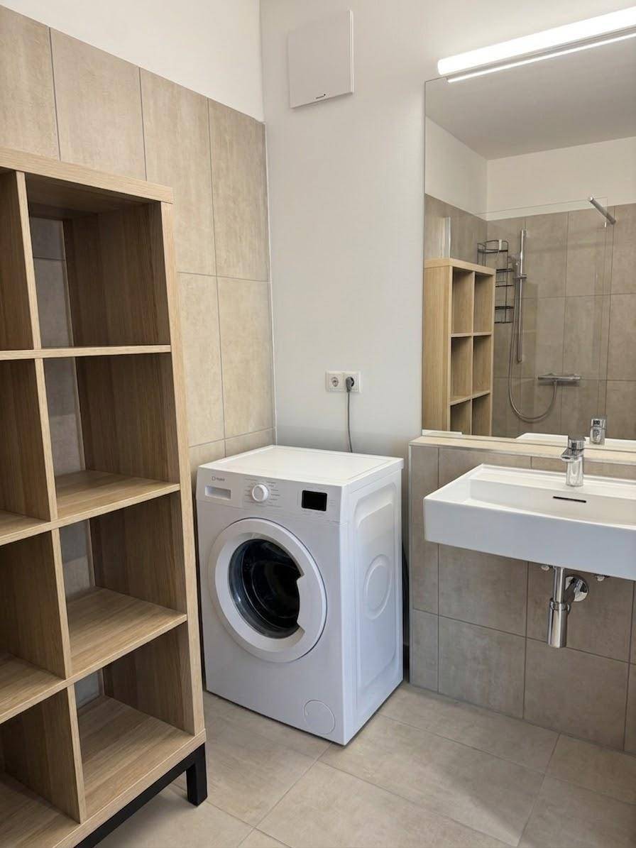 Modernes Badezimmer mit Waschmaschine, Waschbecken und hellen Fliesen.