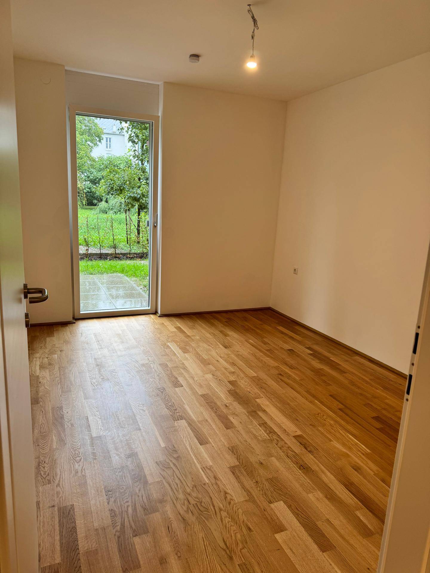 Helles Zimmer mit Holzboden und Zugang zum Garten, ideal für ein Schlafzimmer.