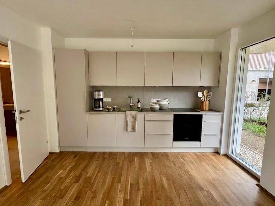 Moderne Küchenzeile mit hellgrauen Schränken, Holzboden und viel Tageslicht.
