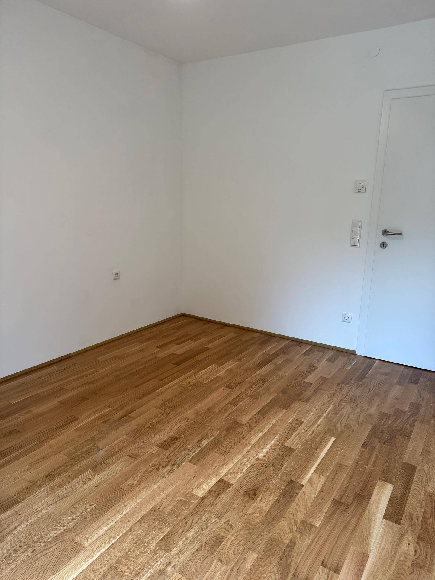 Leeres Zimmer mit Holzboden und weißen Wänden, bereit zur individuellen Einrichtung.