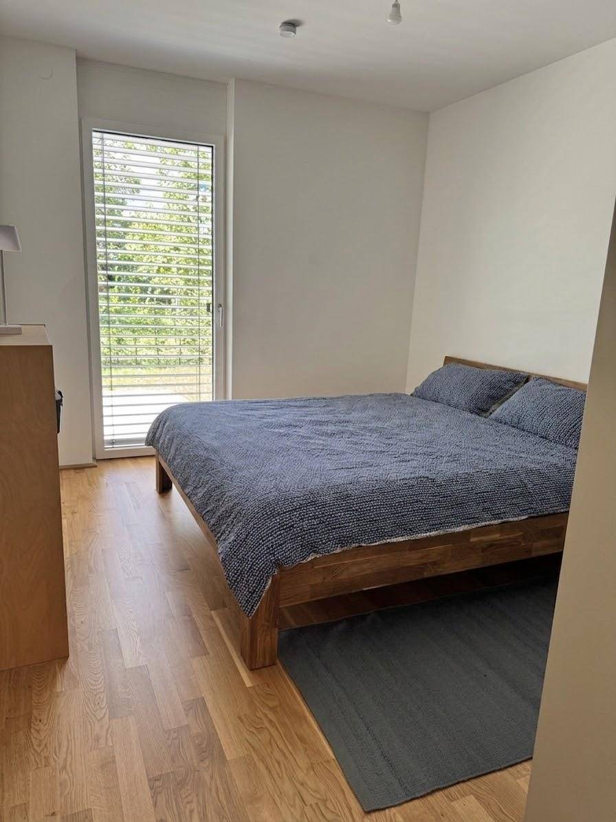 Schlafzimmer mit Holzbett, blauem Bettzeug und großem Fenster für viel Tageslicht.