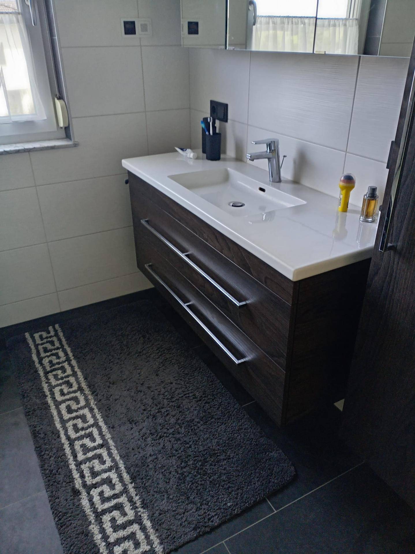 Modernes Badezimmer mit Einzelwaschbecken, dunklem Holzunterschrank und Fenster.