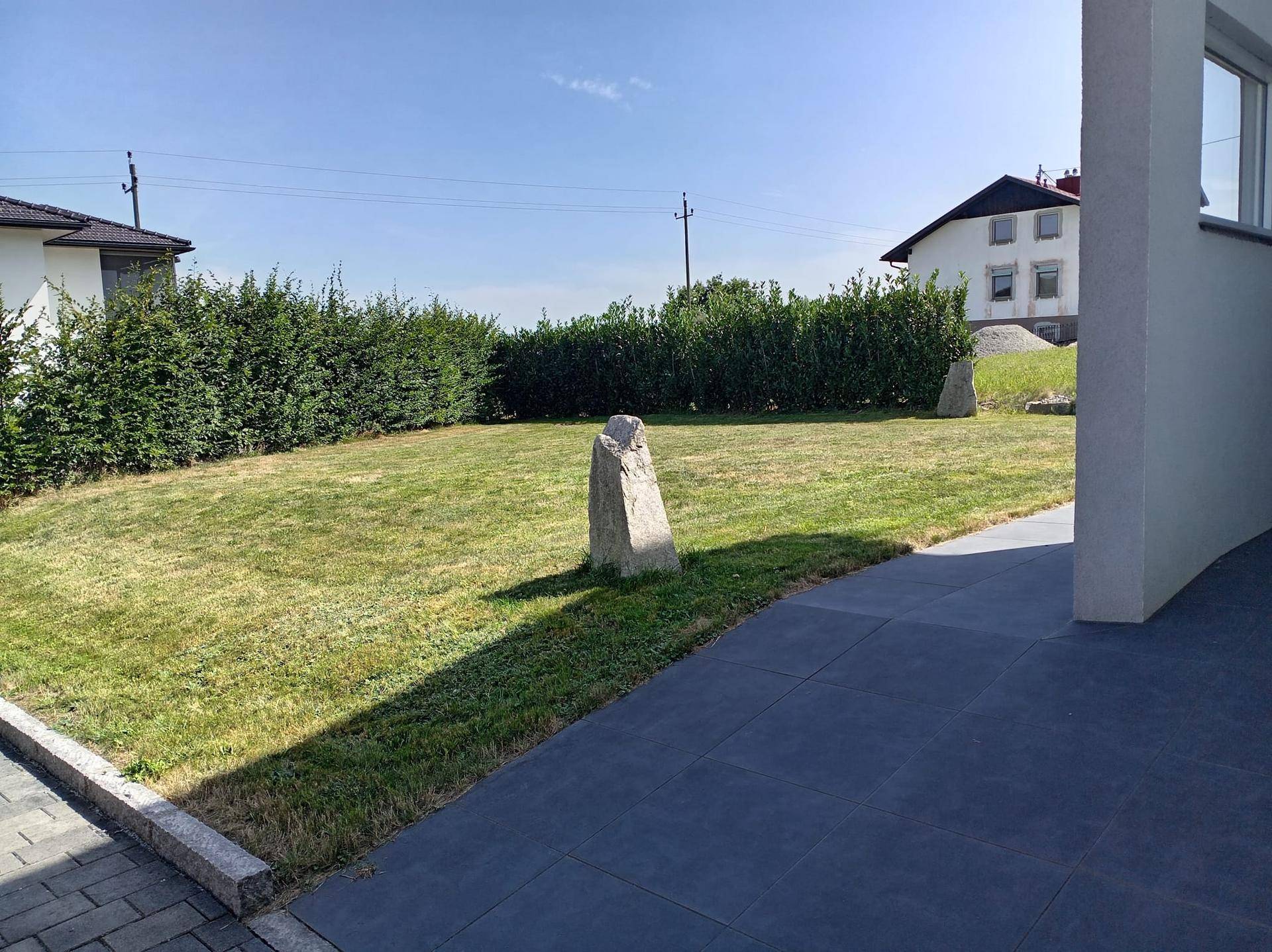 Große Rasenfläche im Vorgarten mit Hecke und dekorativen Steinen.