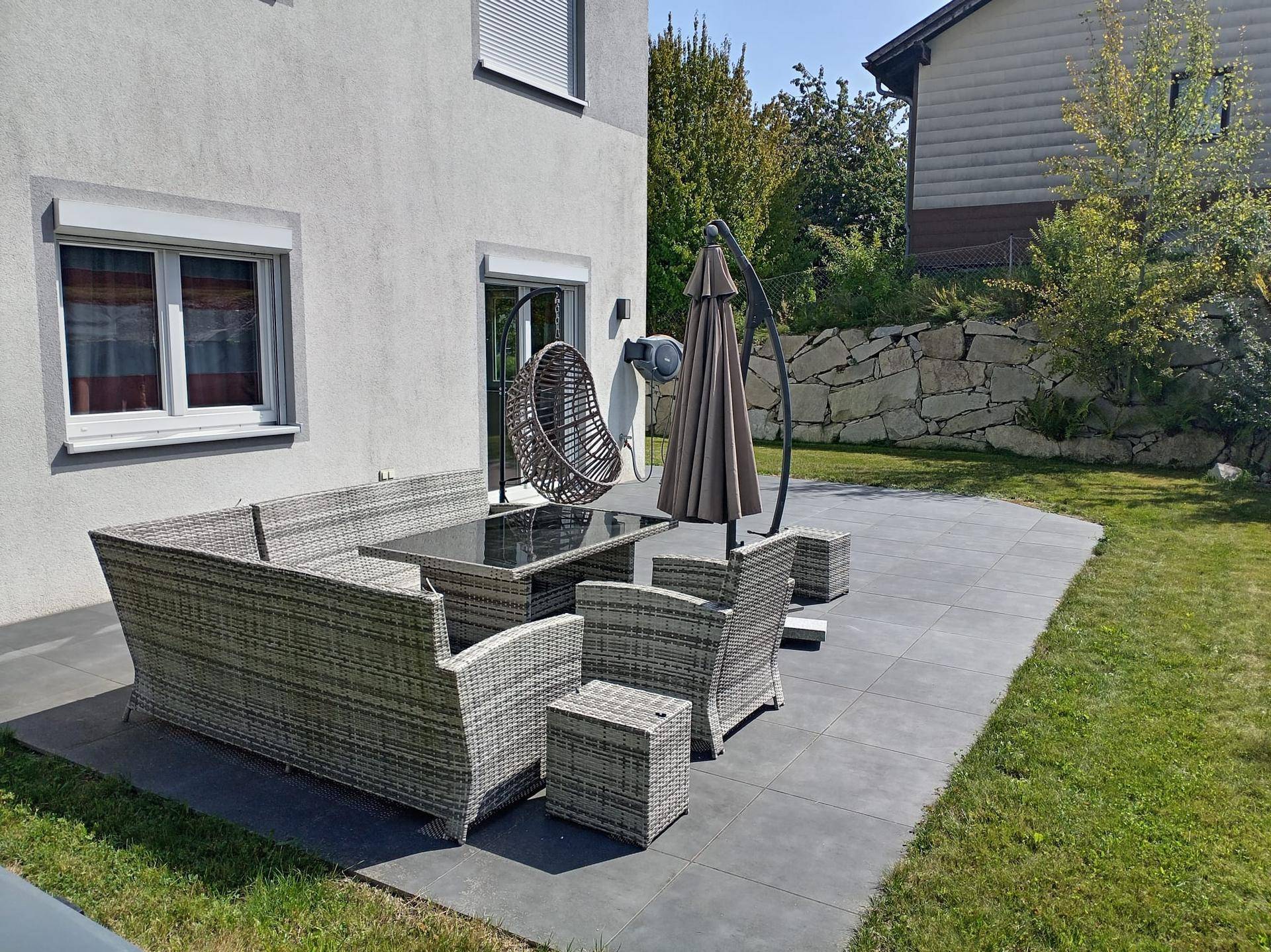 Große Terrasse mit Rattan-Sitzgruppe, Sonnenschirm und Zugang zum Garten.