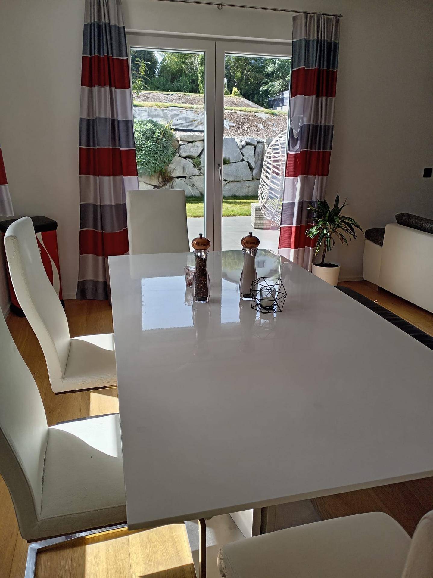 Heller Essbereich mit großem weißen Esstisch, modernen Stühlen und Blick in den Garten.
