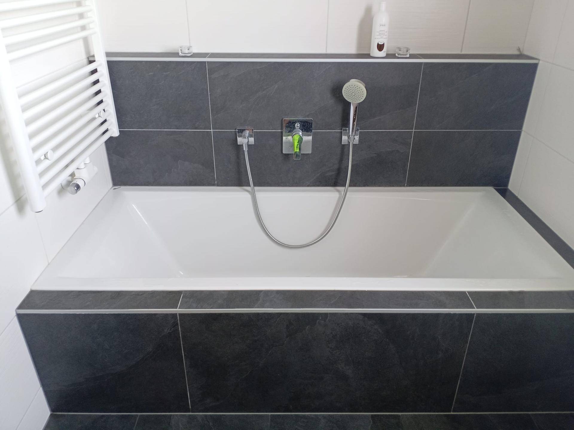 Eingebaute Badewanne mit dunkler Fliesenverkleidung und weißem Handtuchheizkörper.