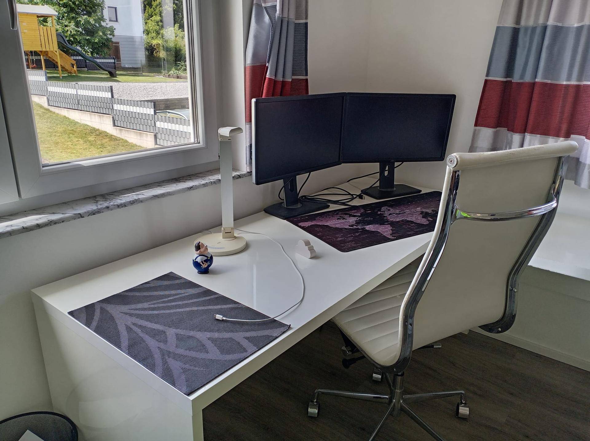 Heller Arbeitsplatz mit zwei Monitoren, weißem Schreibtisch und Blick ins Grüne.