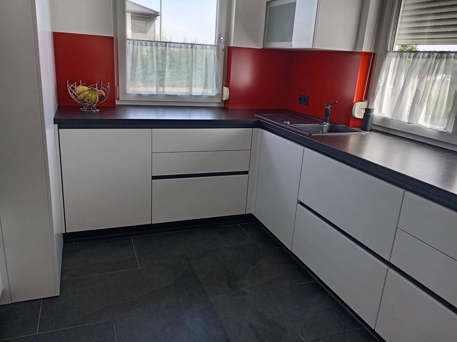 Detailansicht der modernen Küche mit Spülbecken, dunkler Arbeitsplatte und rotem Spritzschutz.
