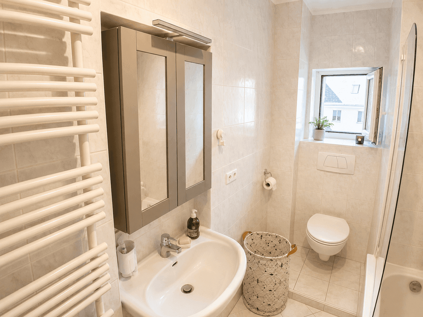 Gefliestes Badezimmer mit Waschbecken, Toilette, Duschbereich und einem beheizten Handtuchhalter.