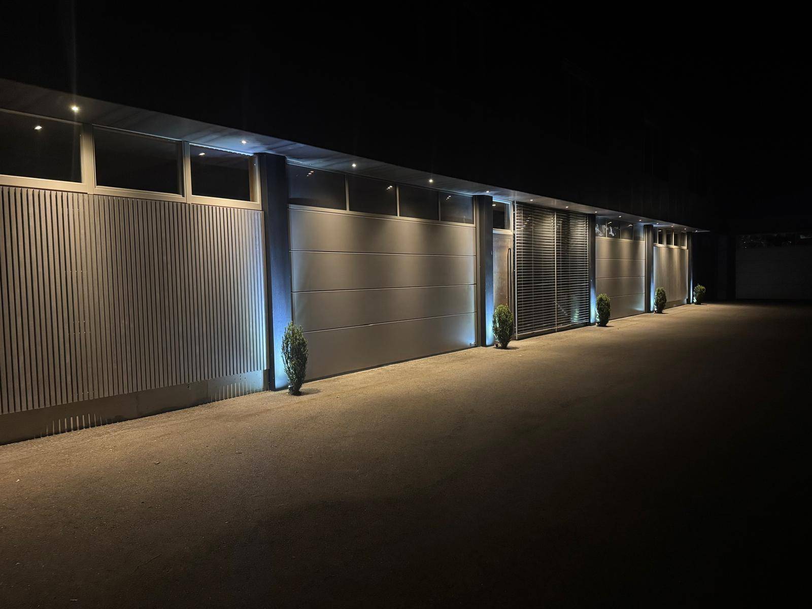 Seitenansicht der modernen Gewerbefassade bei Nacht mit akzentuierter Beleuchtung der Garagentore.