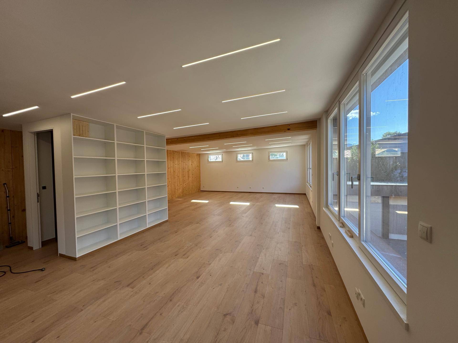 Geräumiger, heller Bürobereich mit Holzboden, großen Fenstern und moderner Deckenbeleuchtung.