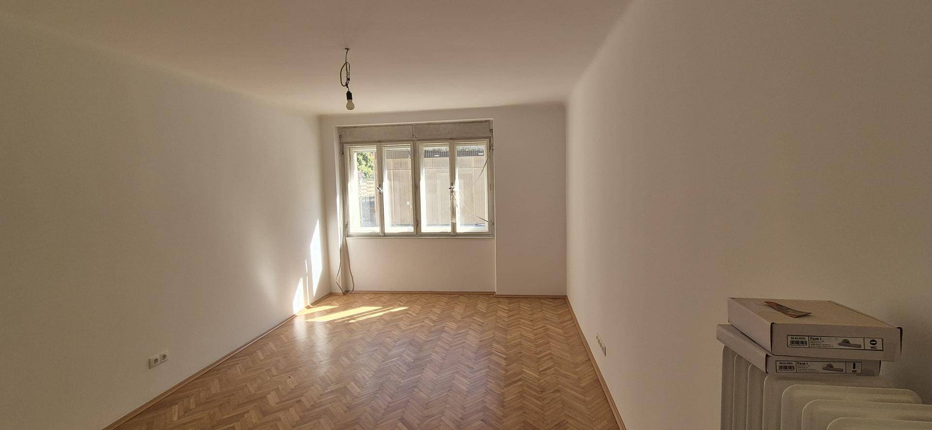 Heller Raum mit Fischgrätparkett, weiß gestrichenen Wänden und einem Fenster.