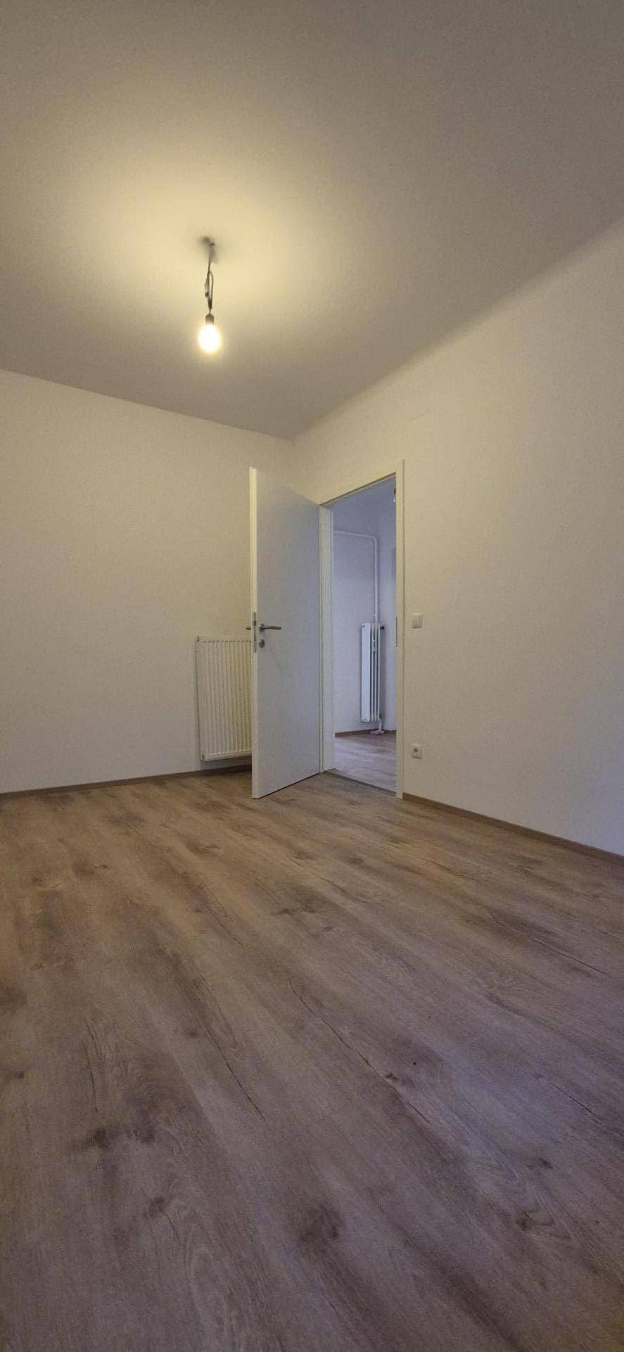 Leerer Raum mit Laminatboden, weiß gestrichenen Wänden und offener Tür zu einem weiteren Zimmer.