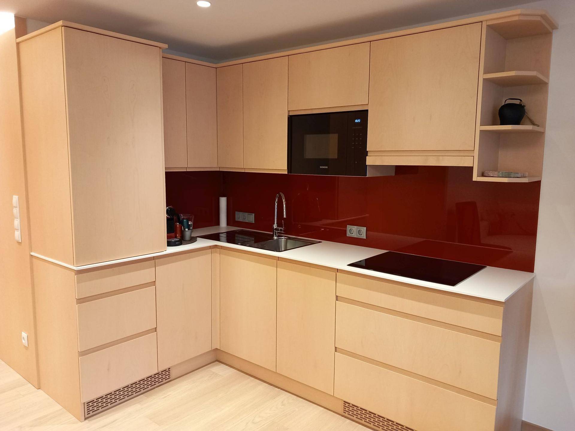 Moderne Einbauküche mit hellen Holzfronten, roter Glasrückwand und Induktionskochfeld.