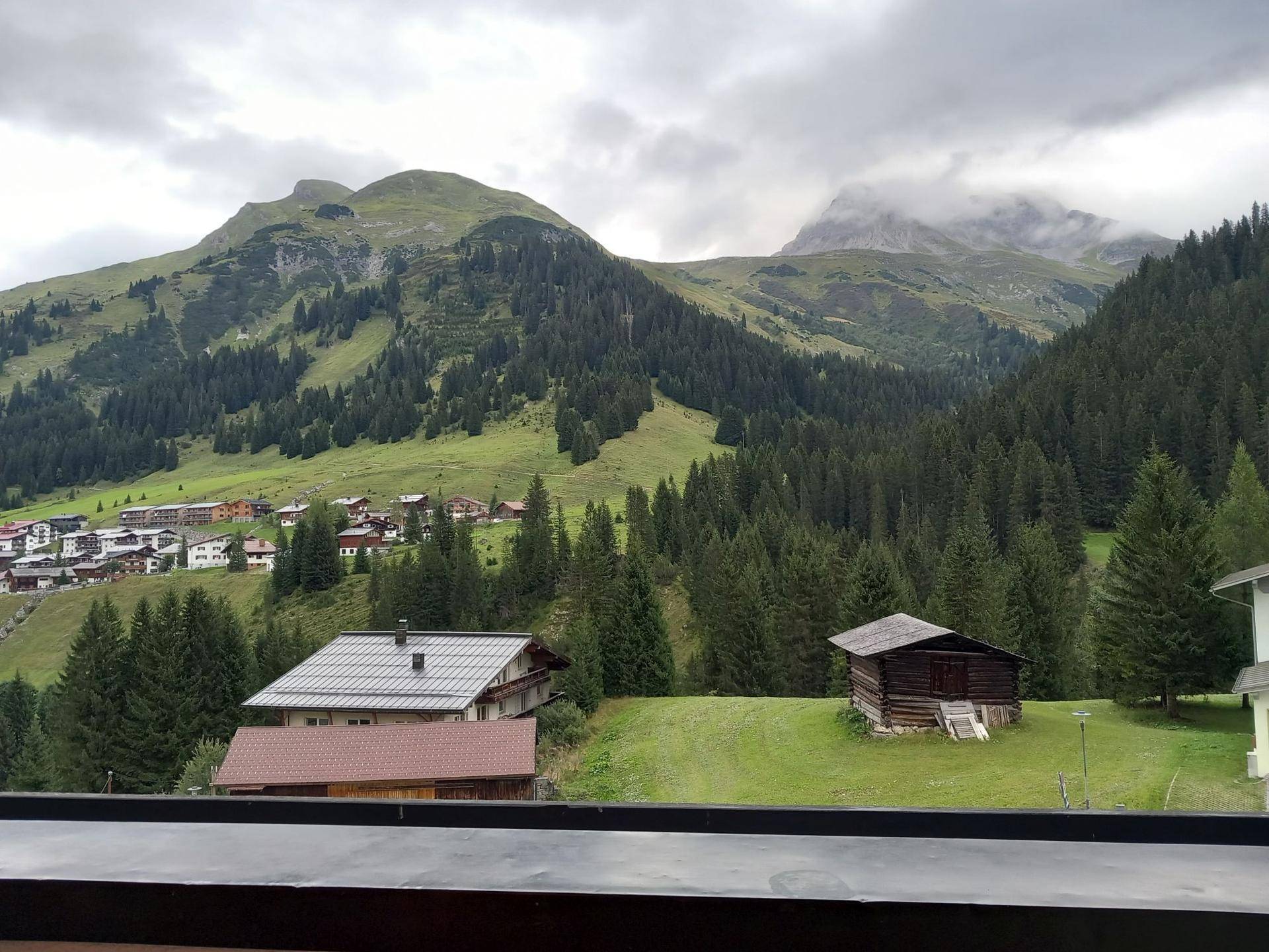 Panoramablick auf grüne Berge, Wälder und traditionelle Häuser in alpiner Landschaft.