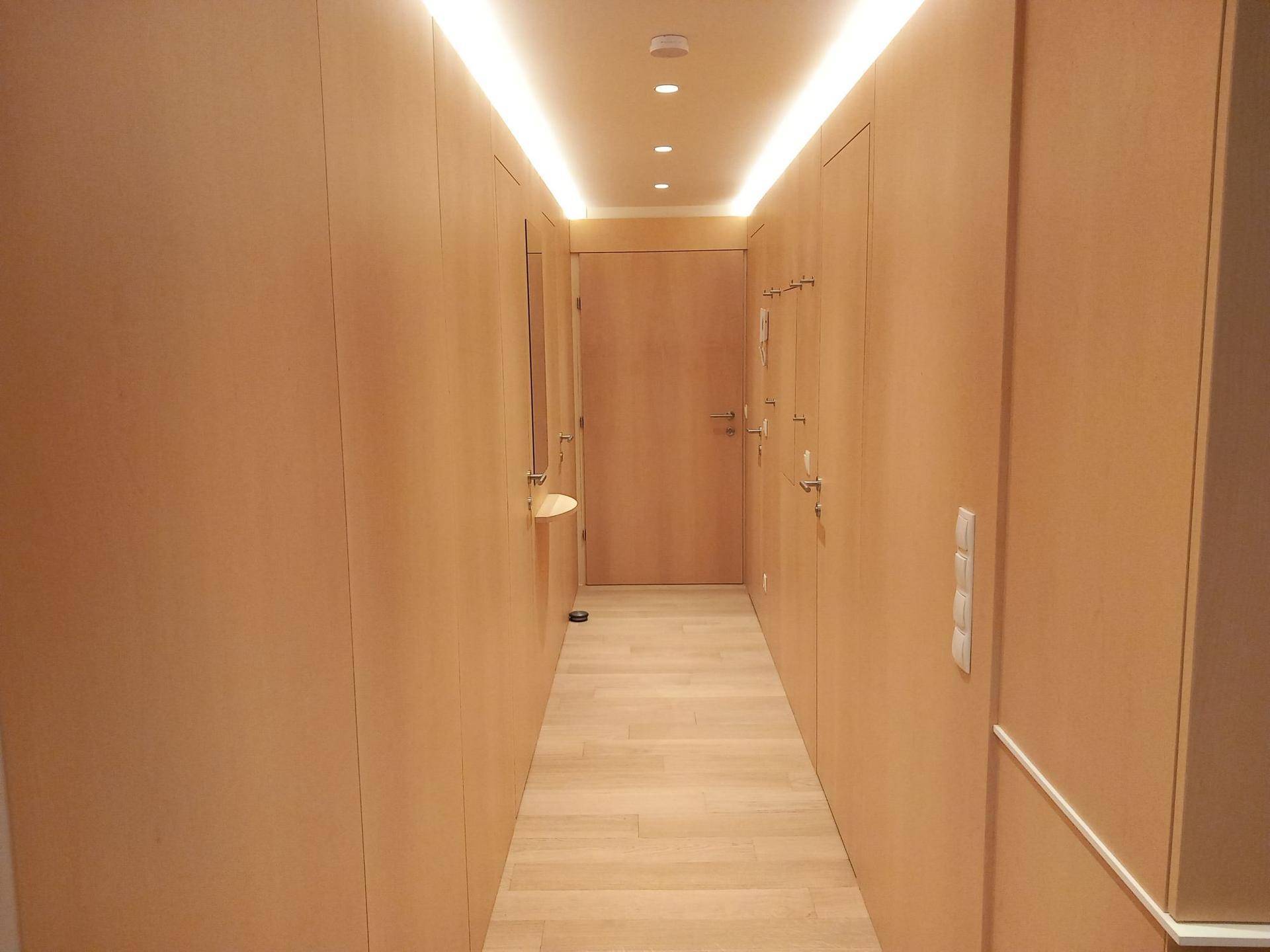 Heller Flur mit Holzverkleidung, integrierter Beleuchtung und Garderobe.