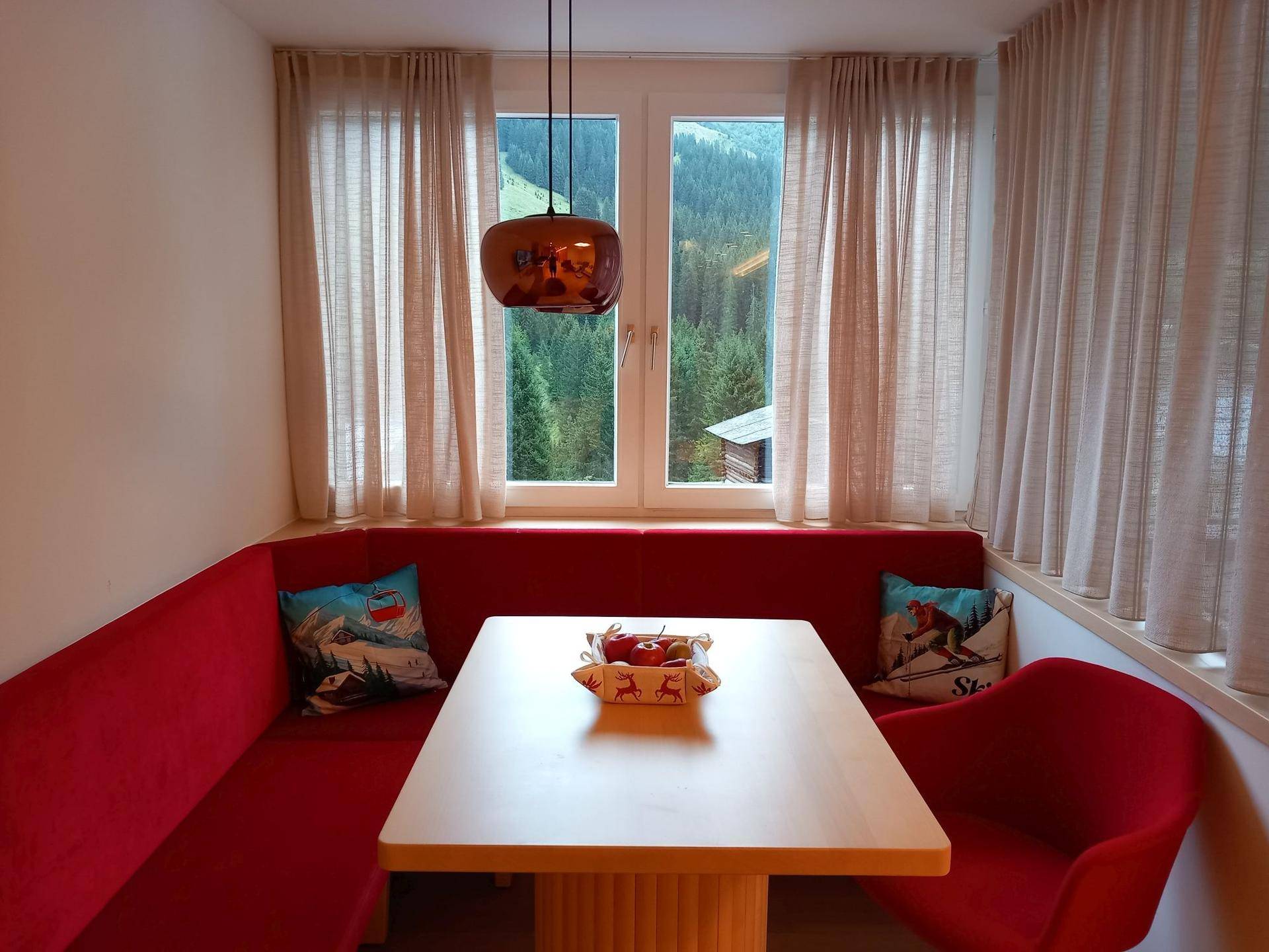 Gemütliche Essecke mit roter Eckbank, Holztisch und Blick auf die Berge.