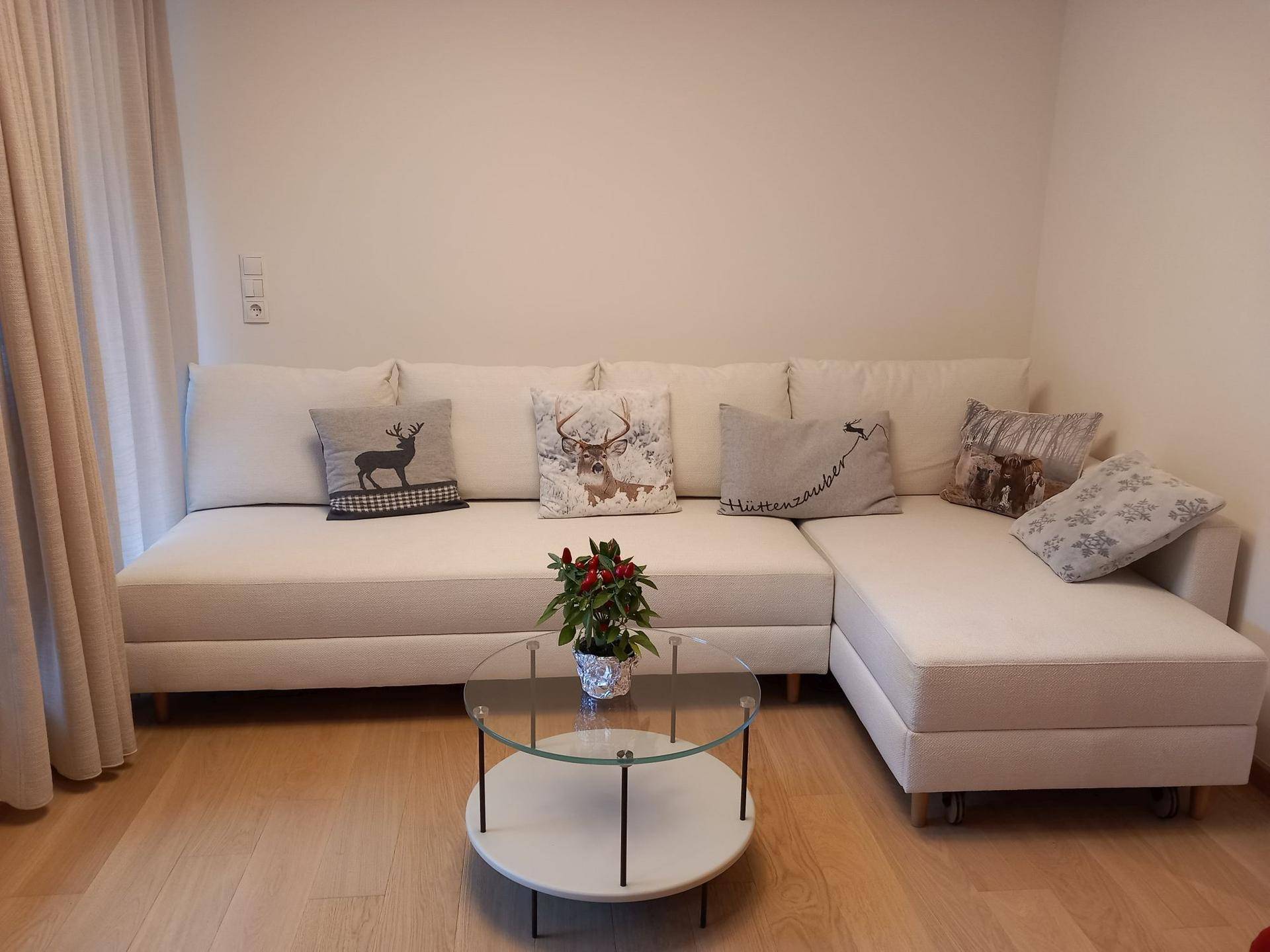 Helles Wohnzimmer mit beigem Ecksofa, Couchtisch und alpinen Dekokissen.